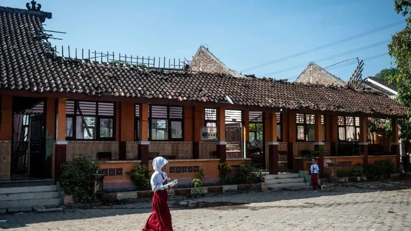 Siswa berjalan membawa paket Makan Bergizi Gratis (MBG) dekat ruang kelas yang atapnya ambruk di SD Negeri Tanggirejo, Tegowanu, Grobogan. (ANTARA FOTO/Aprillio Akbar).