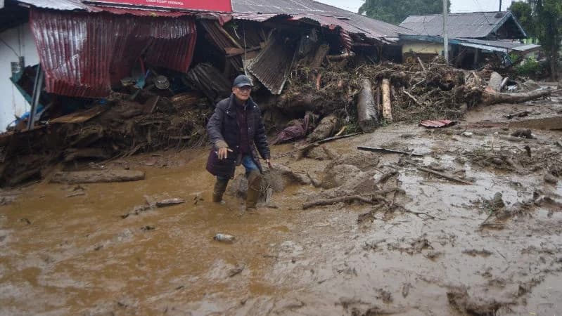 Warga berjalan melewati material banjir bandang di Arosuka, Kabupaten Solok, Sumatera Barat.