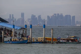 Sejumlah wisatawan turun dari kapal motor dengan latar gedung-gedung tinggi Singapura di pelabuhan objek wisata Pulau Belakang Padang, Batam,