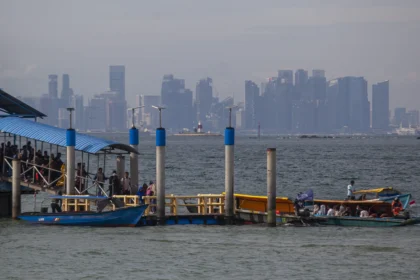 Sejumlah wisatawan turun dari kapal motor dengan latar gedung-gedung tinggi Singapura di pelabuhan objek wisata Pulau Belakang Padang, Batam,