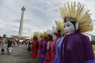 Warga melihat Ondel-Ondel yang dipajang pada Karnaval Sarendo-Rendo 2025 di kawasan Monas, Jakarta, Minggu (14/12/2025).