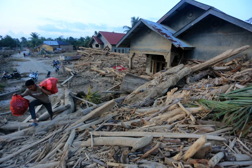 Warga melintasi kayu gelondongan yang terbawa arus banjir di Desa Geudumbak, Kecamatan Langkahan, Aceh Utara, Aceh