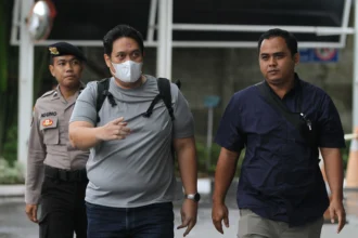 Kepala Kejaksaan Negeri (Kajari) Hulu Sungai Utara (HSU) Albertinus P. Napitupulu (tengah) dikawal petugas saat tiba di Gedung Merah Putih KPK usai terjaring operasi tangkap tangan (OTT), Jakarta, Jumat (19/12/2025)