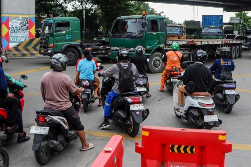 Pengendara sepeda motor berhenti saat truk melintas di Jalan Raya Cilincing, Jakarta