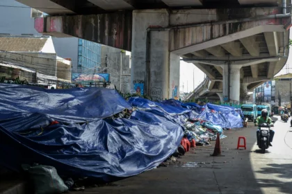 Pengendara motor melintas di samping tumpukan sampah yang ditutupi terpal di Ciputat, Tangerang Selatan, Banten, Selasa (16/12/2025).