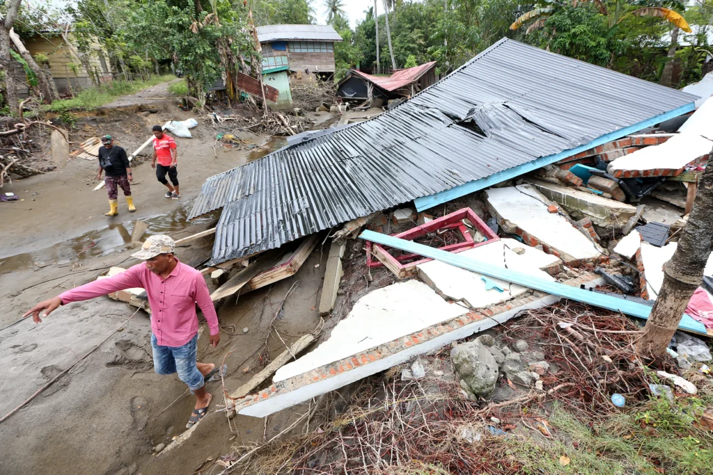 Warga melintas di dekat rumah yang hancur akibat bencana banjir bandang di Desa Alue Kuta, Kecamatan Jangka, Bireuen, Aceh