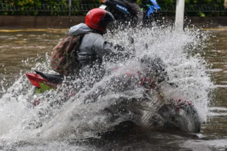 Pengendara sepeda motor menerobos banjir di Jalan Ahmad Yani, Cempaka Putih, Jakarta