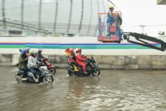 Pekerja proyek menaiki alat berat saat melintasi banjir rob di Jalan R.E Martadinata, Tanjung Priok, Jakarta Utara