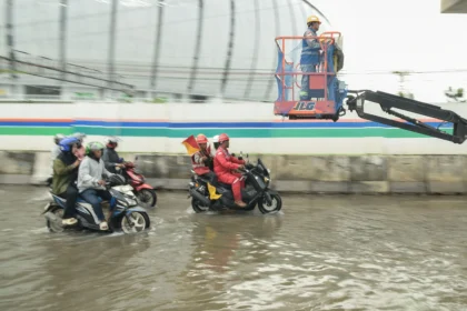 Pekerja proyek menaiki alat berat saat melintasi banjir rob di Jalan R.E Martadinata, Tanjung Priok, Jakarta Utara