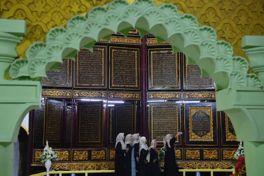 Wisatawan berswafoto dengan latar belakang ukiran ayat-ayat Al Quran yang dipajang di Al Quran Al Akbar, Gandus, Palembang, Sumatera Selatan