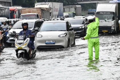 Petugas Kepolisian (kanan) mengatur lalu lintas kendaraan yang terjebak kemacetan saat melintasi genangan air di Cawang, Jakarta