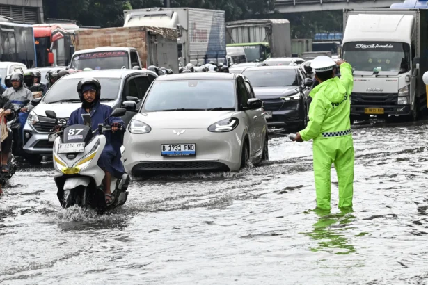 Petugas Kepolisian (kanan) mengatur lalu lintas kendaraan yang terjebak kemacetan saat melintasi genangan air di Cawang, Jakarta