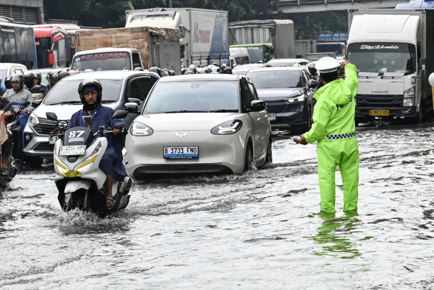 Petugas Kepolisian (kanan) mengatur lalu lintas kendaraan yang terjebak kemacetan saat melintasi genangan air di Cawang, Jakarta