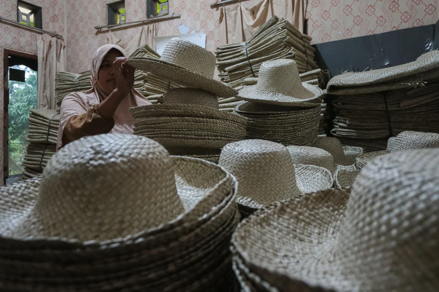 Perajin merapikan topi anyaman daun pandan yang belum terjual di Desa Medong, Mekarjaya, Pandeglang, Banten, Senin (2/3/2026). Sebanyak 157 perajin topi anyaman daun pandan dari dua kecamatan di Pandeglang terancam kehilangan mata pencaharian setelah kerja sama ekspor dengan perusahaan mitra dihentikan sejak Februari 2026, sementara pasar lokal belum mampu menyerap produk dalam jumlah besar seperti permintaan pasar ekspor. (ANTARA FOTO/Angga Budhiyanto/nz)