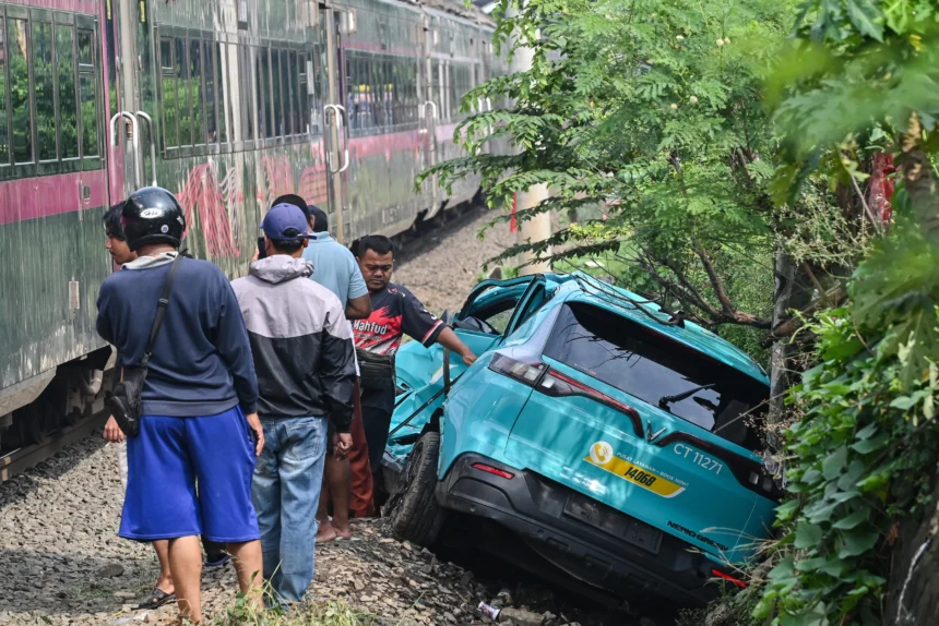 Kereta api (KA) jarak jauh melintas di samping taksi listrik Green SM yang rusak pascakecelakaan KRL Commuter Line dan KA Argo Bromo Anggrek di Stasiun Bekasi Timur, Bekasi. (Sumber: Antara Foto/Fakhri Hermansyah/nz)