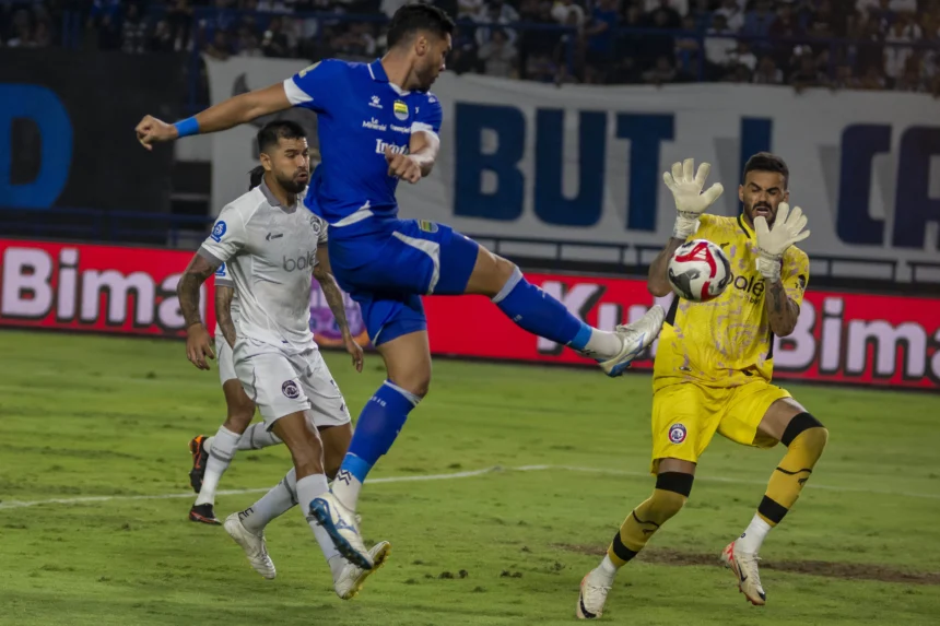 Pesepak bola Persib Bandung Julio Cesar De Freitas Filho (tengah) menendang bola dan berupaya dihalau penjaga gawang Arema FC Lucas Henrique Frigeri pada pertandingan lanjutan BRI Super League di Stadion Gelora Bandung Lautan Api (GBLA), Bandung, Jawa Barat