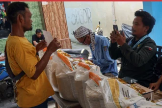 Petugas memotret identitas penerima bantuan sosial saat penyaluran beras dan MinyaKita di Kelurahan Sukamaju, Kota Depok, Jawa Barat