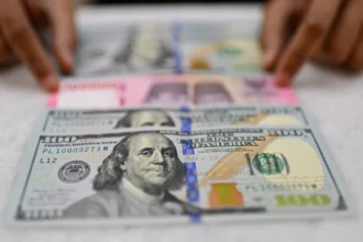 Karyawan memperlihatkan uang pecahan rupiah dan dolar Amerika Serikat (AS) di gerai penukaran mata uang asing Ayu Masagung, Jakarta, Selasa (12/5/2026).