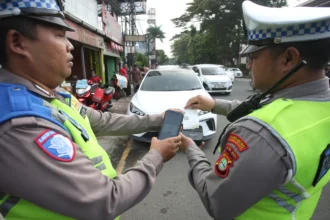 Petugas Satlantas Polres Metro Tangerang Kota mencetak bukti tilang elektronik menggunakan perangkat tilang elektronik portabel (ETLE Handheld) terhadap kendaraan yang melanggar larangan parkir di Jalan Daan Mogot, Tangerang, Banten, Kamis (7/5/2026).
