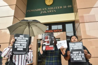 Aktivis KontraS membentangkan poster tuntutan usai Tim Advokasi untuk Demokrasi (TAUD) menyerahkan surat permintaan penghentian persidangan kasus dugaan penyiraman air keras terhadap aktivis KontraS Andrie Yunus di halaman Pengadilan Militer II-08 Jakarta, Senin (8/6/2026).