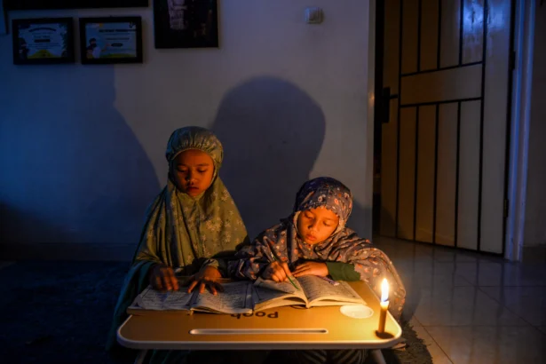 Dua anak mengaji menggunakan penerangan lilin saat pemadaman listrik bergilir di Cinunuk, Kabupaten Bandung, Jawa Barat, Jumat (19/6/2026).