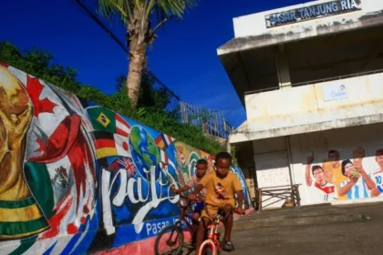 Ilustrasi warga Papua bermain sepeda berlatar belakang mural Piala Dunia 2026 di Jayapura.