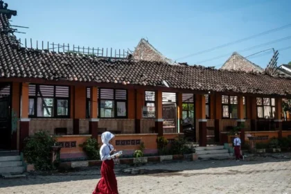 Siswa berjalan membawa paket Makan Bergizi Gratis (MBG) dekat ruang kelas yang atapnya ambruk di SD Negeri Tanggirejo, Tegowanu, Grobogan. (ANTARA FOTO/Aprillio Akbar).