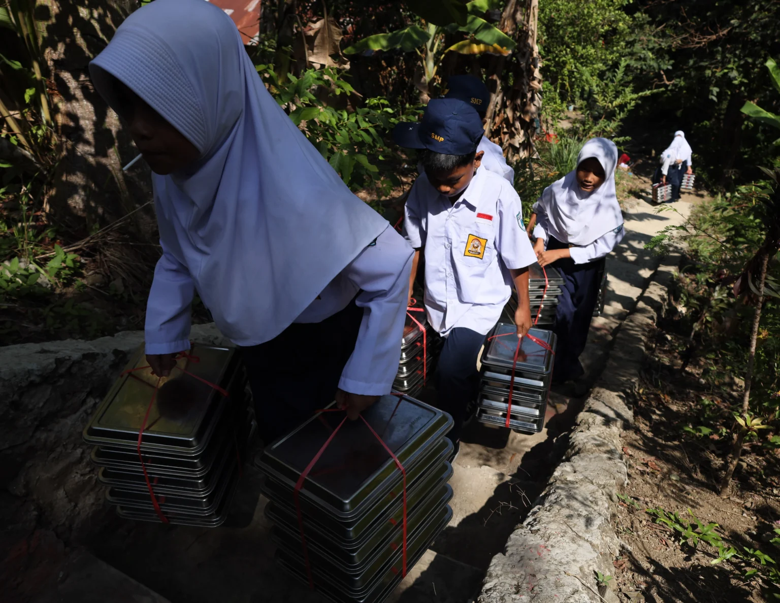 Sejumlah siswa membawa ompreng Program Makan Bergizi Gratis (MBG) yang akan disalurkan ke sekolah, di Sangkurio, Mamuju, Sulawesi Barat, Selasa (11/8/2026).