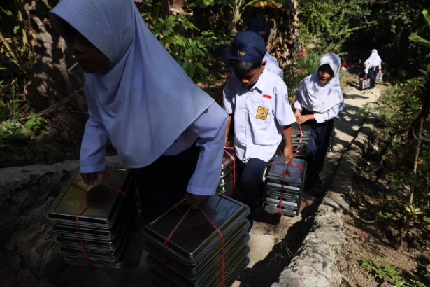 Sejumlah siswa membawa ompreng Program Makan Bergizi Gratis (MBG) yang akan disalurkan ke sekolah, di Sangkurio, Mamuju, Sulawesi Barat, Selasa (11/8/2026).