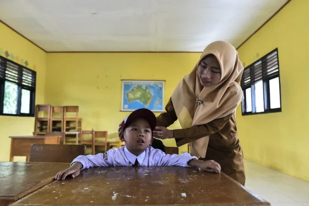 Guru merapikan topi siswa kelas 1 yang merupakan anak-anak transmigran saat kegiatan belajar mengajar di SDN 44/III Sungai Bermas, Kerinci, Jambi. (Sumber: Antara Foto/Wahdi Septiawan/agr)