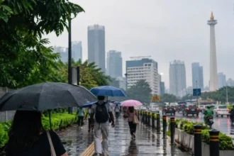 Ilustrasi warga memakai payung saat huja gerimis di Jakarta.