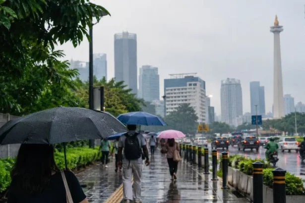 Ilustrasi warga memakai payung saat huja gerimis di Jakarta.