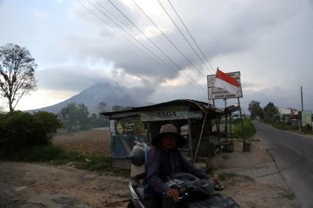 Warga mengendarai sepeda motor dengan latar Gunung Sinabung yang erupsi di Kecamatan Naman Teran, Kabupaten Karo, Sumatera Utara