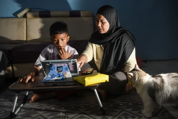 Siswa Sekolah Dasar Negeri 07 Rorotan Pagi, Richie Archilles (kiri), didampingi orang tuanya mengikuti pembelajaran secara daring dari rumah di Jakarta Utara, Senin (7/9/2026).