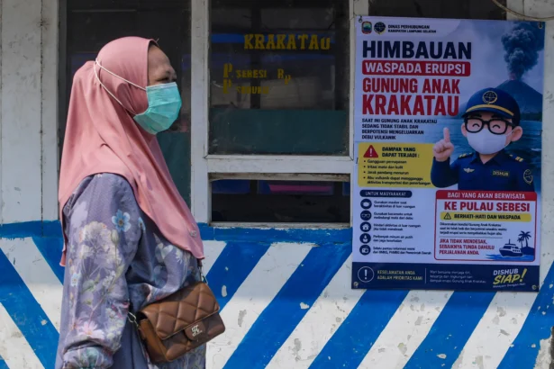 Warga berjalan di dekat spanduk imbauan waspada erupsi Gunung Anak Krakatau di Dermaga Canti, Rajabasa, Kabupaten Lampung Selatan, Lampung